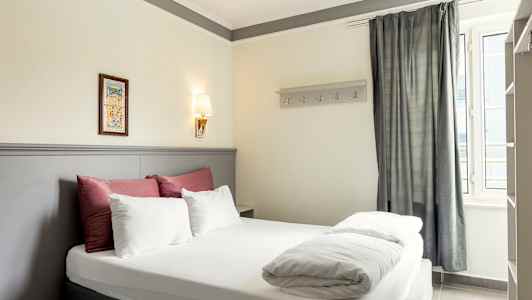 Kuva hotellihuoneesta, jossa on parivuode, koristeltu valkoisilla ja punaisilla vuodevaatteilla sekä vaaleanharmaa sängynpääty. (Tekoälyn luoma teksti)