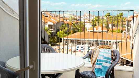 Näkymä parvekkeelta, jossa on pöytä ja tuolit, kohti loma-alueen uima-aluetta ja rakennuksia. (Tekoälyn luoma teksti)