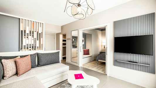 Tilava ja modernisti sisustettu hotellihuone, jossa istuinryhmä, makuutila ja seinälle kiinnitetty TV. (Tekoälyn luoma teksti)