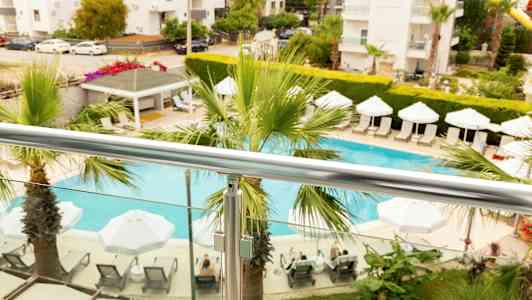 Näkymä parvekkeelta, jossa on uima-allas, aurinkovarjoja ja aurinkotuoleja, ympärillä kasveja. (Tekoälyn luoma teksti)