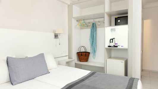 Hotellihuone, jossa sänky, vaatekaappi ja pieni jääkaappi. (Tekoälyn luoma teksti)