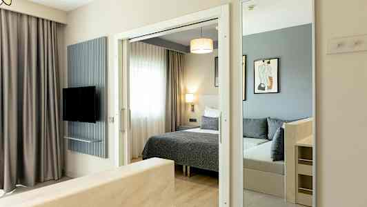 Kuva hotellihuoneesta, jossa on sänky, peili ja televisio. (Tekoälyn luoma teksti)