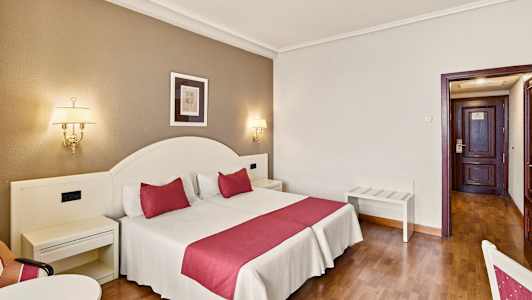 Hotellihuone, jossa on parivuode punaisilla yksityiskohdilla, seinälamput ja ovi taustalla. (Tekoälyn luoma teksti)