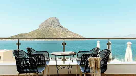 Neljä tuolia ja pöytä terassilla, josta on näkymä merelle ja vuorenhuipulle. (Tekoälyn luoma teksti)