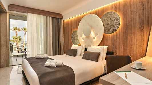 Hotellihuone, jossa on suuri sänky, koristelu seinä ja avoin parveke näkymällä. (Tekoälyn luoma teksti)