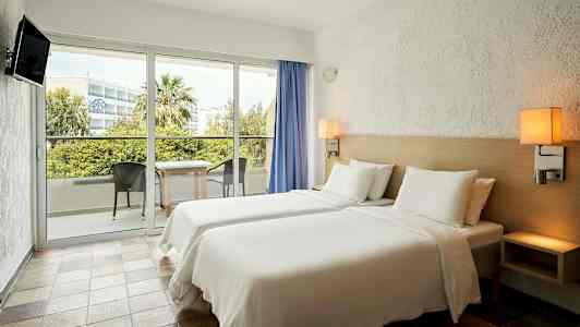 Hotellihuone, jossa kaks sänkyä, parveke ja näkymä vihreisiin alueisiin. (Tekoälyn luoma teksti)