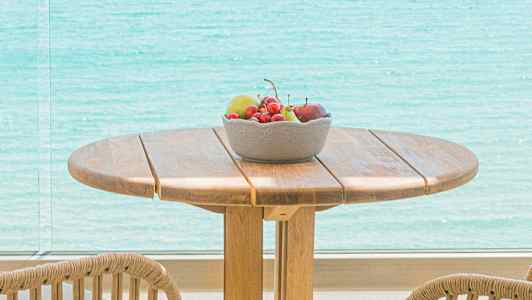 Puiset pöytä ja tuolit, kulho hedelmiä ja näkymä merelle. (Tekoälyn luoma teksti)