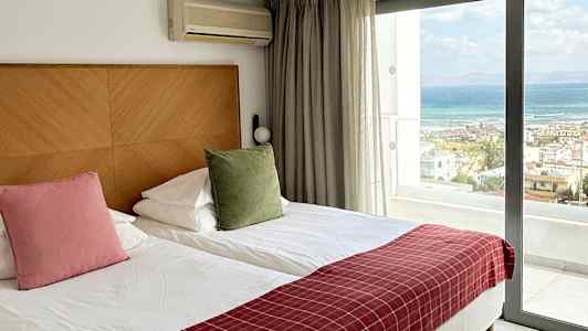 Hotellihuone, jossa kaksi erillistä vuodetta, suuri lasiovi näkymällä merelle ja mukavuuksia kuten ilmastointi. (Tekoälyn luoma teksti)