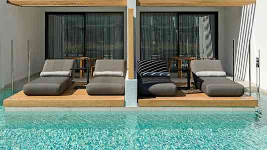 Ylelliset aurinkotuolit uima-altaan äärellä nykyaikaisten hotellihuoneiden edessä. (Tekoälyn luoma teksti)