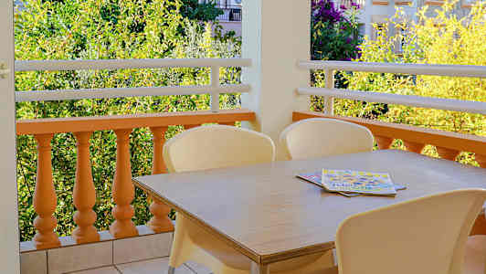 Parvekkeen kuva, jossa on pöytä ja tuolit laattalattialla sekä näkymä vihreään ja rakennuksiin. (Tekoälyn luoma teksti)