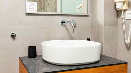 Kylpyhuone, jossa on pyöreä pesuallas puukaapin päällä, peili yläpuolella sekä yksityiskohtia, kuten suihku ja hiustenkuivaaja näkyvissä. (Tekoälyn luoma teksti)