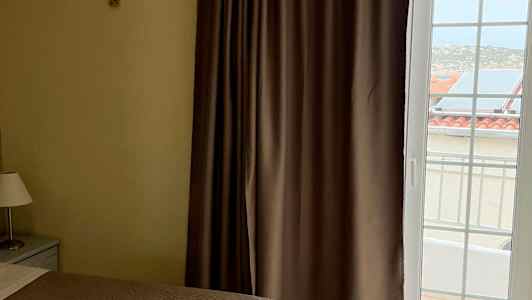 Kaksi sänkyä ruskeilla päiväpeitteillä, ikkuna verhoineen ja näkymä ulkona oleviin rakennuksiin. (Tekoälyn luoma teksti)