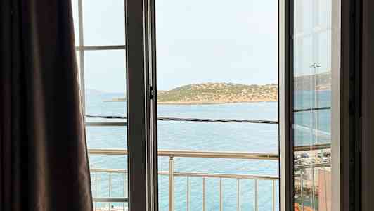 Näkymä avoimesta ikkunasta parvekkeelle, meri ja saari taustalla. (Tekoälyn luoma teksti)