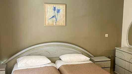 Kaksi erillistä sänkyä ruskeilla päiväpeitteillä, seinällä yläpuolella maalaus ja oikealla lipasto. (Tekoälyn luoma teksti)