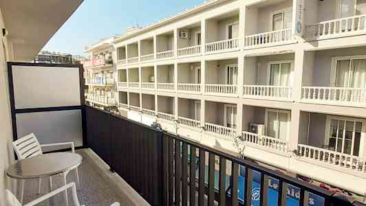 Parveke, jossa on kaksi tuolia ja pöytä, näkymä moderniin rakennukseen. (Tekoälyn luoma teksti)