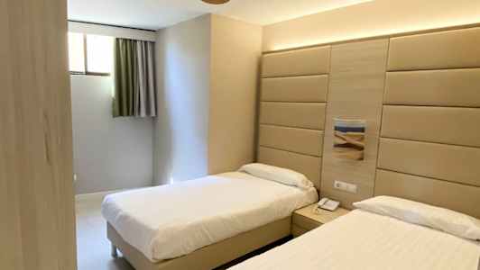 Hotellihuone, jossa on kaksi erillistä sänkyä, seinäpaneeli sänkyjen takana ja kattotuuletin. (Tekoälyn luoma teksti)