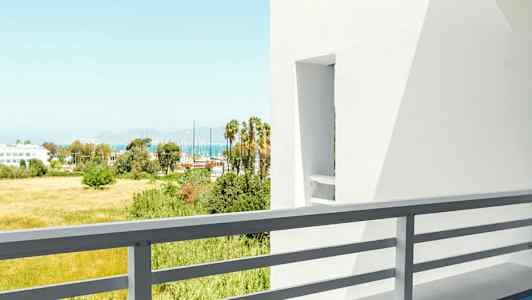 Näkymä parvekkeelta, jossa on pöytä ja tuoli, valkoisia rakennuksia ja vihreää taustalla. (Tekoälyn luoma teksti)