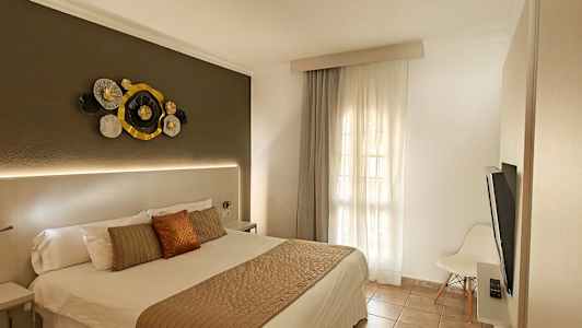 Hotellihuone, jossa on parivuode, koristeellista seinätaidetta sängynpäädyn yläpuolella ja ikkuna vaaleilla verhoilla. (Tekoälyn luoma teksti)