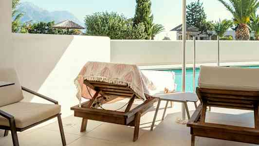 Kuva terassista, jossa on aurinkotuoleja, varjo ja uima-allas taustalla. (Tekoälyn luoma teksti)