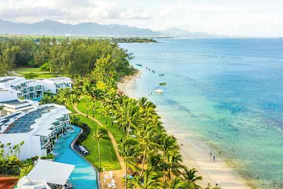 Rannikkonäkymä, jossa on valkoisia rakennuksia, palmuja, hiekkaranta ja turkoosia merta. (Tekoälyn luoma teksti)