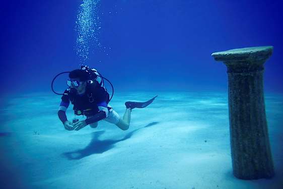 Sukeltaja veden alla lähellä muinaista pylvästä merenpohjassa. (Tekoälyn luoma teksti)