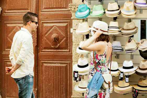 Henkilö kokeilee hattua myyntipöydän ääressä, jossa on erilaisia hattuja. (Tekoälyn luoma teksti)