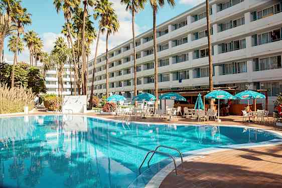 Ulkouima-allas, jossa on aurinkotuoleja ja aurinkovarjoja suuren hotellin edessä. (Tekoälyn luoma teksti)