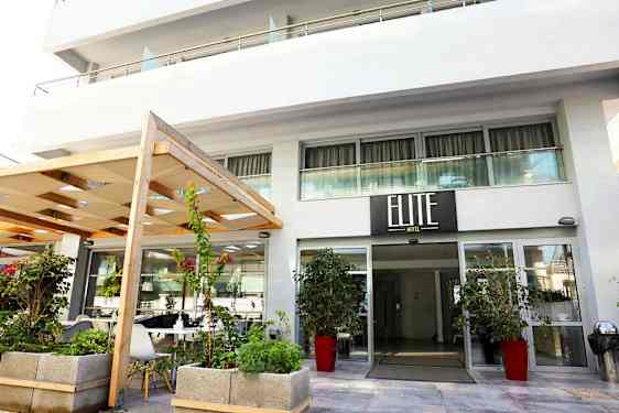 Hotellin sisäänkäynti, jossa kyltti 'Elite Hotel', ympäröitynä kasveilla ja kukilla. (Tekoälyn luoma teksti)