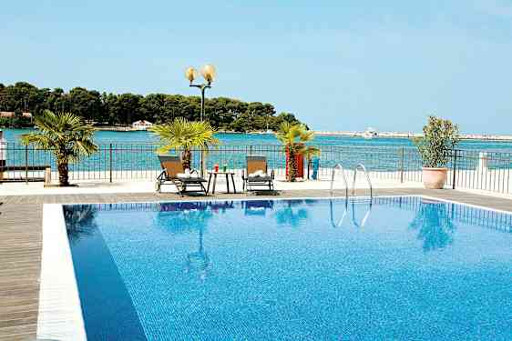 Uima-allas, jossa kirkasta sinistä vettä, ja kaksi aurinkotuolia vieressä. Taustalla näkyy meri. (Tekoälyn luoma teksti)