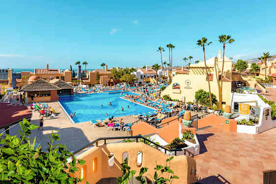 Hotellialue, jossa on suuri uima-allas, aurinkotuoleja ja rakennuksia. (Tekoälyn luoma teksti)