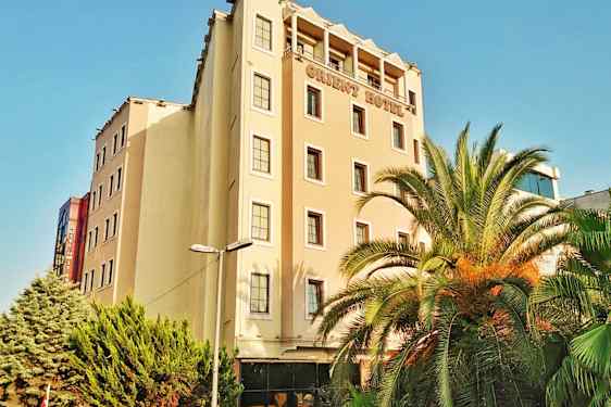 Monikerroksinen hotellirakennus. Rakennuksen edessä on palmuja ja vihreitä puita. (Tekoälyn luoma teksti)