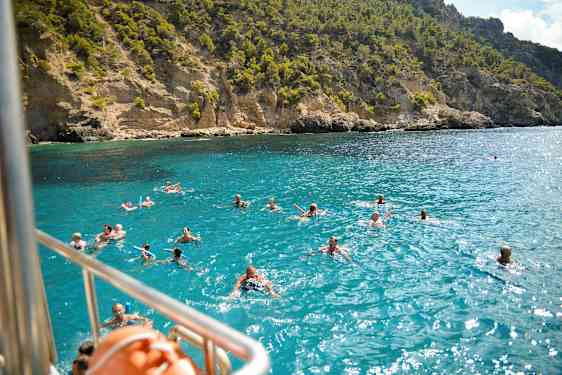 Ihmisiä uimassa kirkkaassa sinisessä vedessä kallioisen rannikon edustalla. (Tekoälyn luoma teksti)