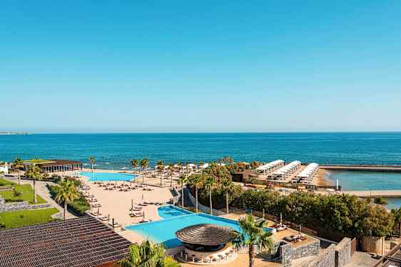 Näkymä lomakeskuksesta, jossa on uima-allas, aurinkotuoleja, palmuja ja taustalla meri. (Tekoälyn luoma teksti)