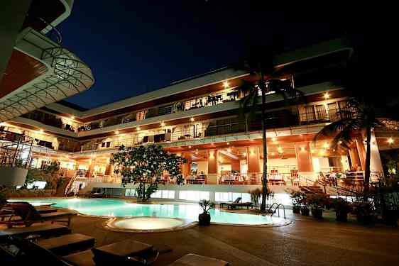 Ilta näkymä monikerroksisesta rakennuksesta, valaistu julkisivu ja uima-allas etualalla. (Tekoälyn luoma teksti)