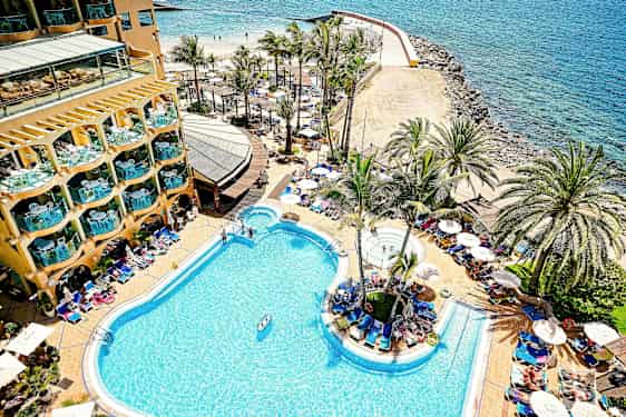 Hotellin uima-allas rannalla, ympärillä palmuja ja aurinkotuoleja. (Tekoälyn luoma teksti)