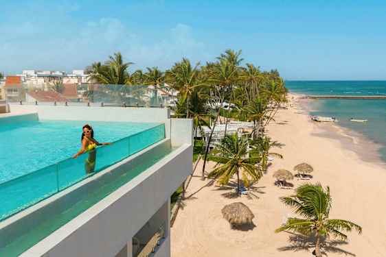 Uima-allas lasikaiteilla rakennuksessa, josta on näkymä rannalle palmuineen ja taivaansiniseen mereen. (Tekoälyn luoma teksti)