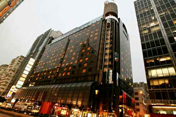 Valaistu monikerroksinen rakennus kaupunkimiljöössä, jossa on lasijulkisivu ja etualalla katuelämää. (Tekoälyn luoma teksti)