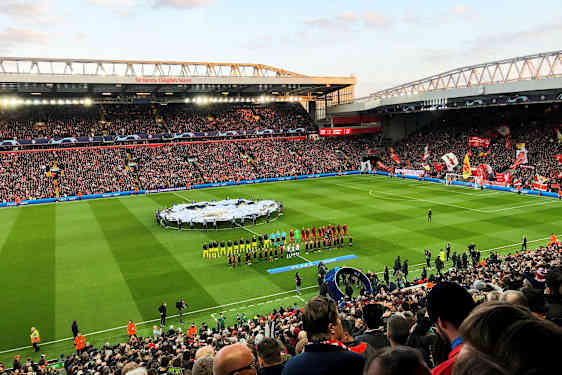 Jalkapallostadion täynnä katsojia, pelaajia ja henkilökuntaa kentällä ennen ottelua. (Tekoälyn luoma teksti)