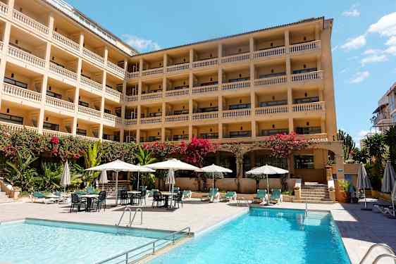 Hotelli, jossa useita kerroksia ja parvekkeita, uima-allasalue aurinkotuoleilla ja aurinkovarjoilla. (Tekoälyn luoma teksti)