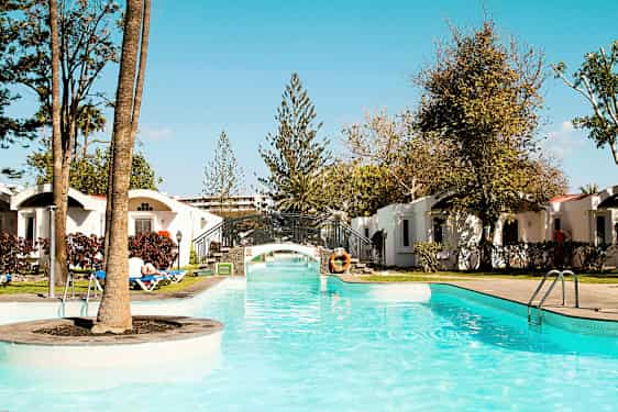 Altaan kirkas vesi ja pieni silta ympäröitynä vehreydellä ja lomamajoilla. (Tekoälyn luoma teksti)