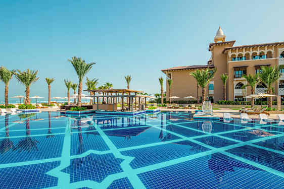 Uima‑allas, jonka reunalla aurinkotuoleja, ympärillä palmuja ja taustalla rakennus. (Tekoälyn luoma teksti)