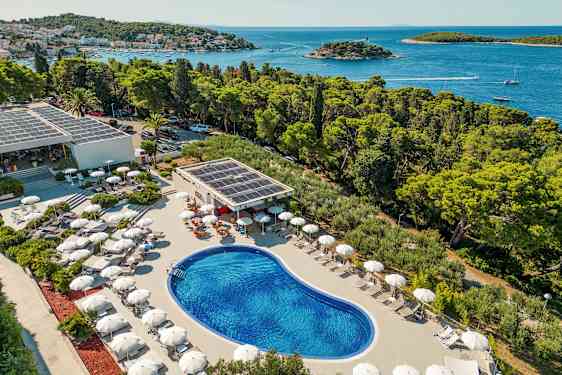 Näkymä ulkouima-altaasta, jota ympäröivät aurinkotuolit ja aurinkovarjot, sijaitsee lähellä rannikkoa metsän ja meren äärellä. (Tekoälyn luoma teksti)