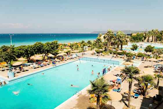 Ulkouima-allas, jonka ympärillä on aurinkotuoleja ja päivänvarjoja, taustalla palmuja ja meri. (Tekoälyn luoma teksti)