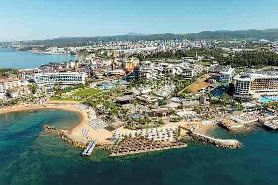 Ilmakuva rannikon lomakylästä, jossa on hotelleja, uima-altaita ja ranta. (Tekoälyn luoma teksti)