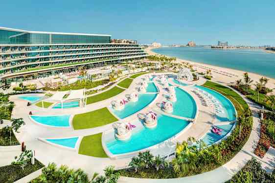 Näkymä lomakohteesta, jossa on useita uima-altaita, viheralueita ja hiekkaranta meren rannalla. (Tekoälyn luoma teksti)