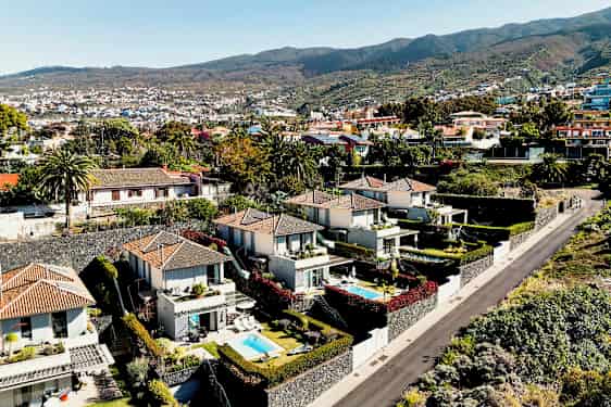 Kuvaus alueesta, jossa on moderneja taloja ja pieniä uima-altaita vihreän ympäröimänä ja tien vieressä. (Tekoälyn luoma teksti)