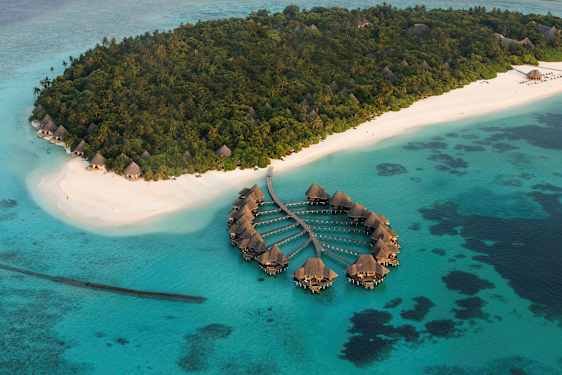 Ilmakuva trooppisesta saaresta, jossa on valkoiset hiekkarannat ja veden ylle rakennettuja huviloita. (Tekoälyn luoma teksti)