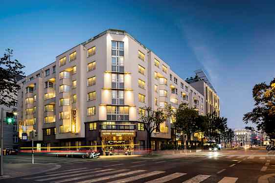 Rakennus valaistuna illalla, useita kerroksia ja ikkunoita, sijaitsee risteyksessä. (Tekoälyn luoma teksti)