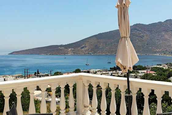 Näkymä terassilta, jossa kaiteet, aurinkovarjo sekä meri ja vuoret taustalla. (Tekoälyn luoma teksti)