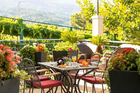 Pöytä, jossa on punaiset tuolit, ympäröitynä vihreillä kasveilla ja värikkäillä kukilla. (Tekoälyn luoma teksti)